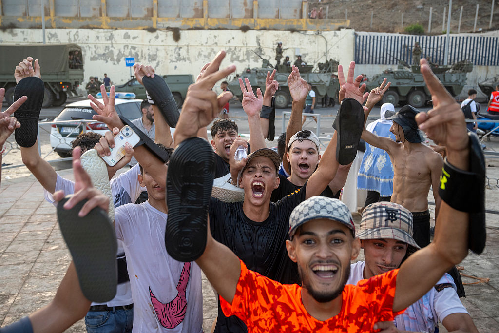 Migrants climbing border fence at Ceuta with Spanish security forces in foreground